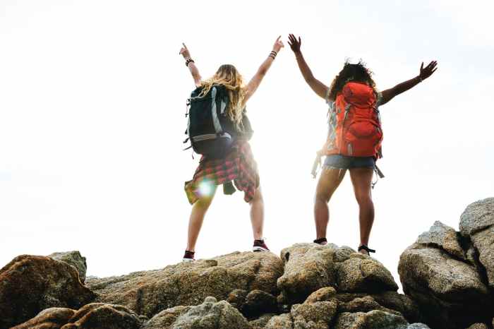 two women in hiking backpacks standing on gray stones